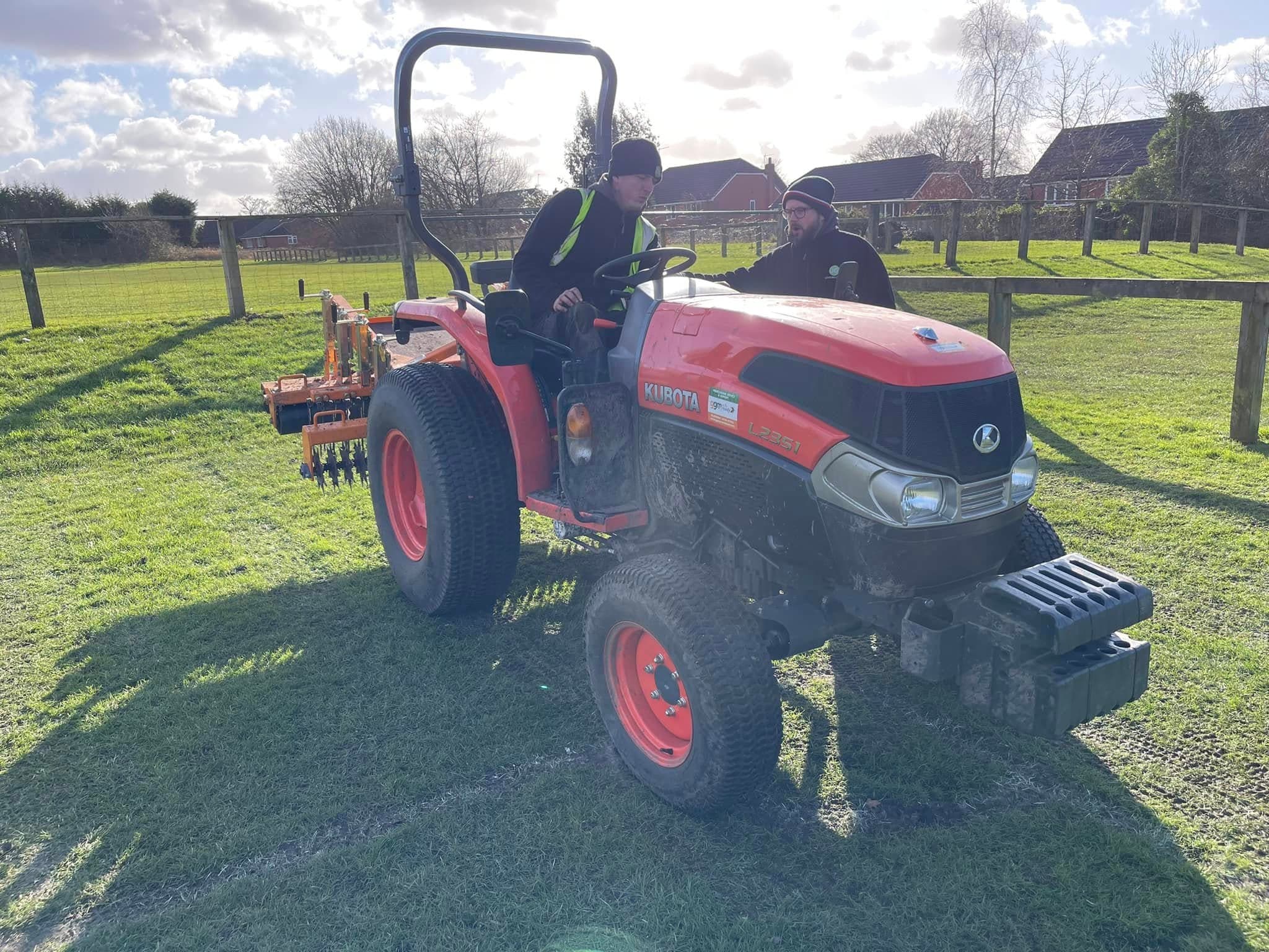 JG operator on a compact tractor pulling a scarifier across a sports pitch