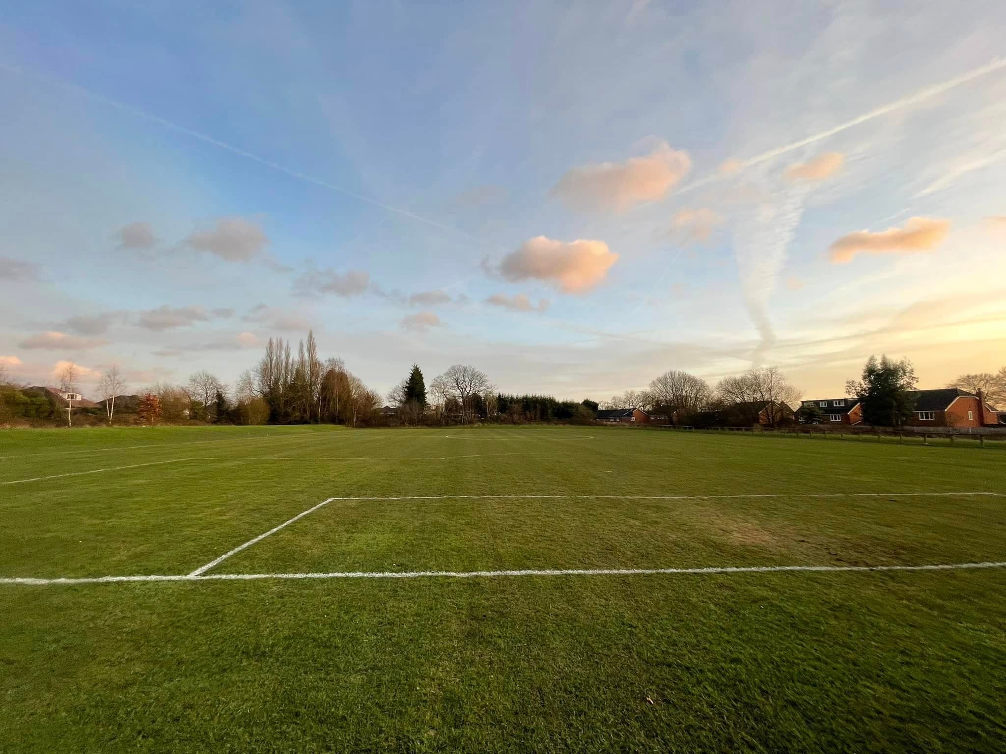 Freshly marked grass pitch under a sunset sky