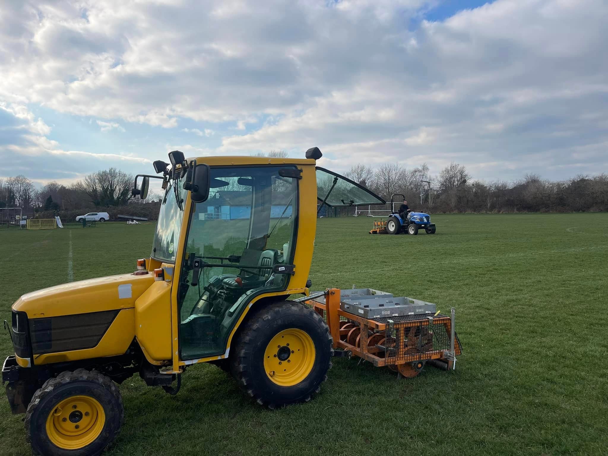 Compact tractor spreading topdressing across a sports field